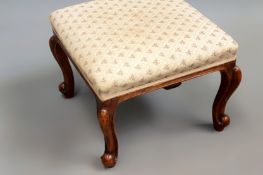 A Victorian upholstered footstool on carved cabriole legs.