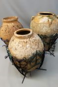 Three terracotta ovoid oil jars in metal framed stands. 96, 86 and 98cm.