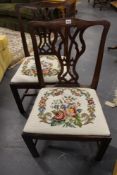 A pair of carved mahogany Georgian chairs. Shaped crest rails above pierced splats. Needlework seats