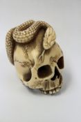 A Japanese carved ivory netsuke modelled in the form of a skull with entwined serpent.