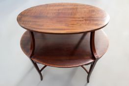 An Edwardian Sheraton style inlaid mahogany two tier occasional table of oval form. Tapered legs