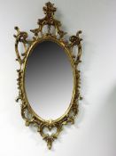 A 19th Century style gilded oval mirror. With rococo style scrolled designs. 124cm high. 54cm wide.