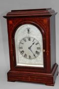 An Edwardian mahogany and inlaid bracket clock. Silvered and engraved arch dial. With Roman numerals