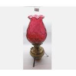 A late 19th/early 20th Century Oil Lamp with cranberry shade over brass font, raised on a base metal