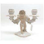 A German Porcelain Two Branch Candlestick, the central support modelled as a cupid, flesh colour and