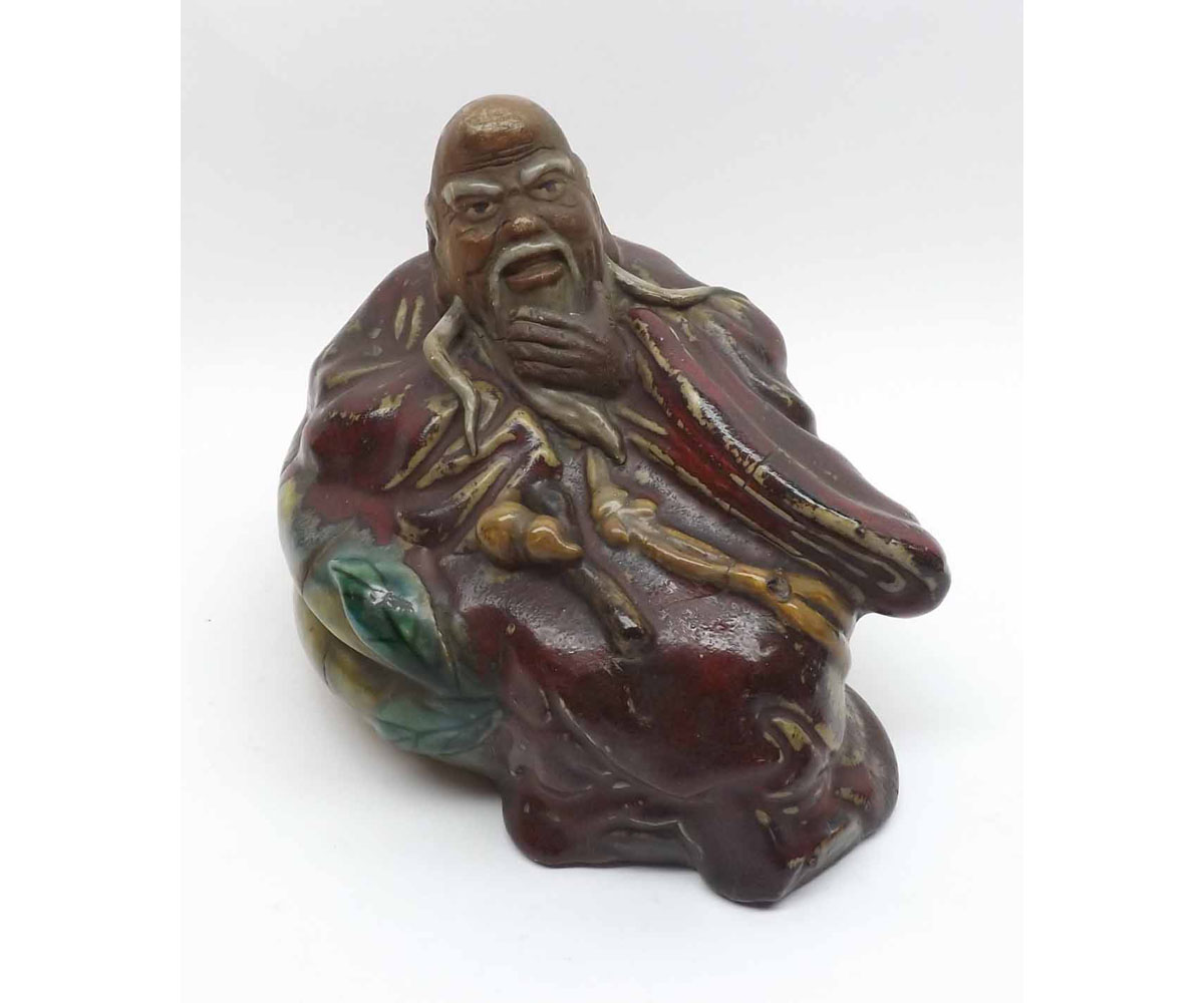A Chinese Pottery Figure of a reclining wise man in a pensive pose, painted predominantly in red