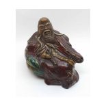 A Chinese Pottery Figure of a reclining wise man in a pensive pose, painted predominantly in red