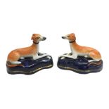 A pair of Staffordshire Models of reclining greyhounds, decorated in typical colours on dark blue