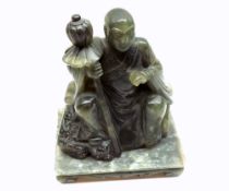 A Chinese Carved Hardstone or Soapstone Seated Figure of a Luohan clutching a staff in his right