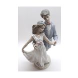A Lladro Group of a young dancing couple, she clutching a posy of flowers in her left hand, 11" high