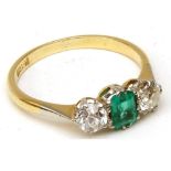 An ungraded yellow metal Ring featuring a centre oval cut Emerald flanked to each side by an Old Cut