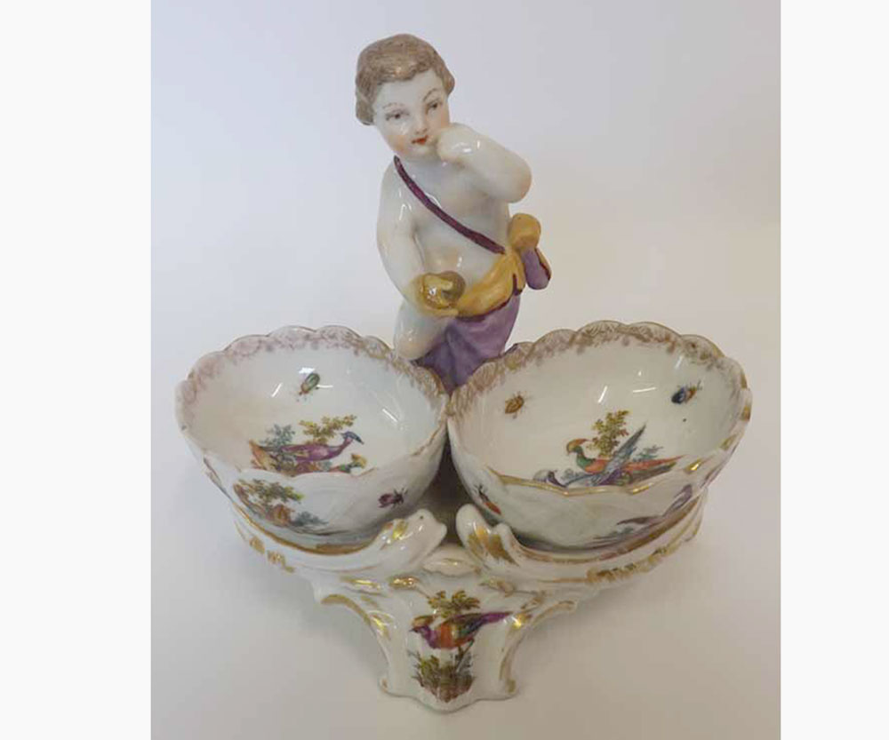 A Berlin Porcelain Cruet, crested with a central figure of a putto, the two bowls each painted in