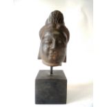 C18th stone head of a Buddha, raised on a wood block