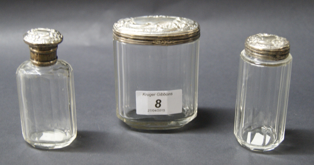 Three repoussé-decorated, hallmarked silver-mounted glass dressing jars.