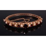A Victorian style 9ct gold garnet and seed pearl set hinged bangle, with safety chain,
