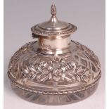 An Edwardian silver mounted glass inkwell, having a finial topped hinged dome cover, the silver