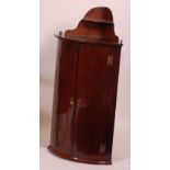 An early 19th century mahogany bowfront hanging corner cupboard, with galleried shelf over,