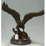 A contemporary cast bronze sculpture of a bird of prey upon a rocky outcrop