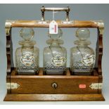 An early 20th century oak three bottle tantalus, with silver plated mounts,