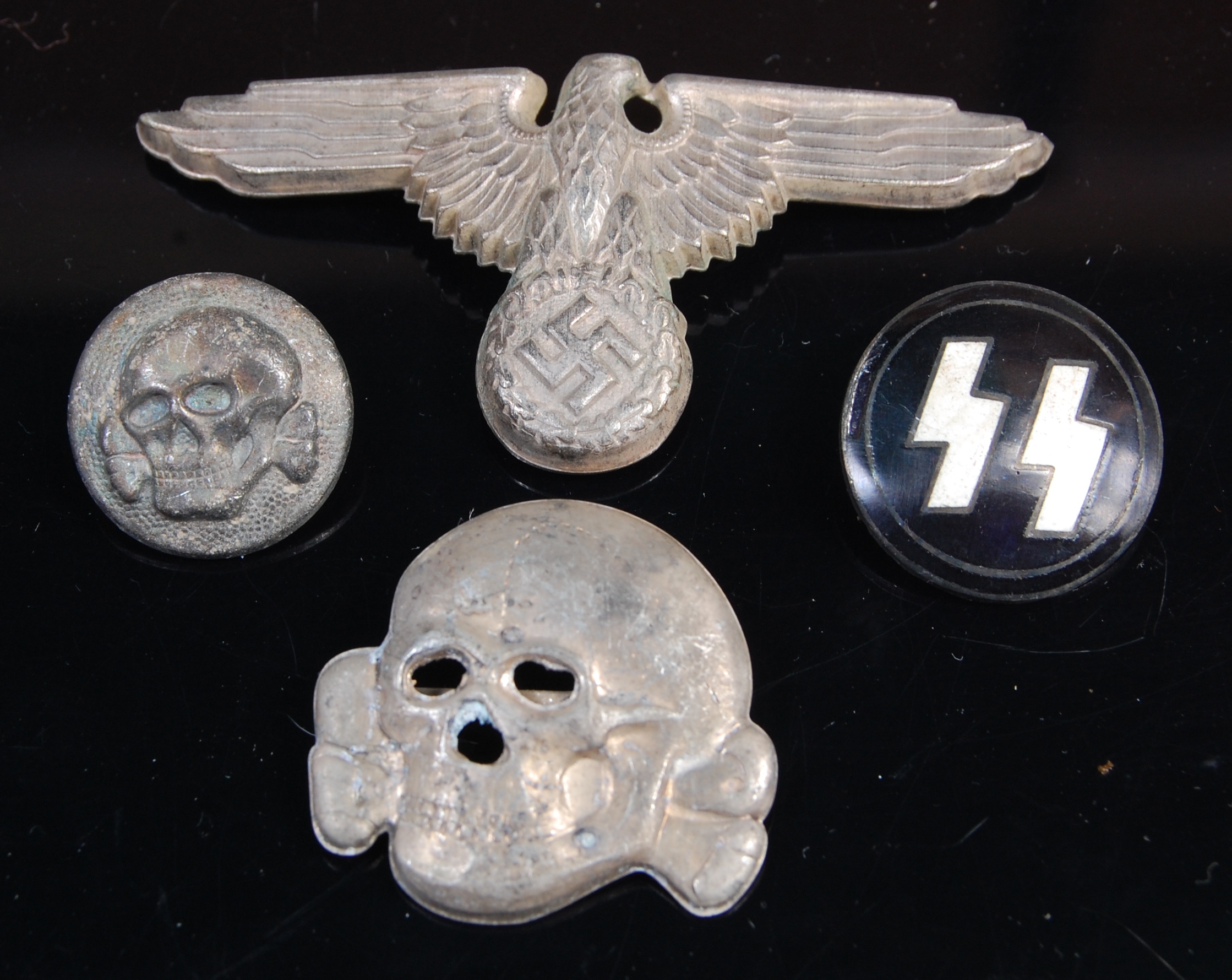 A German Waffen SS spread eagle cap badge, together with three others.