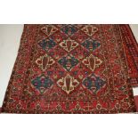 A Persian woollen rug, the rust coloured field decorated with linked medallions within trailing