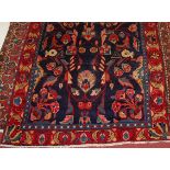 A Persian woollen rug, the blue ground decorated with stylised flowers within trailing borders,