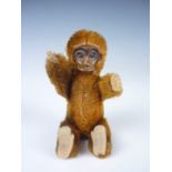 An early 20th Century miniature Schuco monkey, having moulded tin face, cream felt ears, hands and