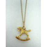 A 9ct gold pendant modelled as a rocking horse with gemstone eyes, on a fine curb link neckchain