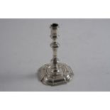 A GEORGE II CAST TAPERSTICK on a square base with rounded corners, a "well" centre and a spool-