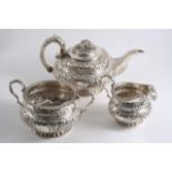 A WILLIAM IV IRISH THREE-PIECE TEA SET of circular form with embossed decoration, scroll handles &