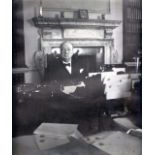 Churchill, Winston Spencer. A signed portrait photograph, sitting at his desk in 10 Downing