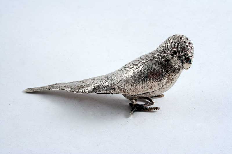 AN EDWARDIAN NOVELTY PEPPERETTE cast in the form of a budgerigar with glass eyes & a hinged base, by