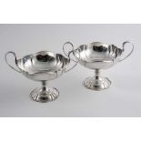 A PAIR OF TWO-HANDLED CUPS on pedestal bases with shaped & moulded rims & bifurcated handles, by