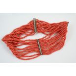A TWELVE ROW UNIFORM CORAL BEAD CHOKER mounted with paste set spacers and clasp, 36.5cm. long.