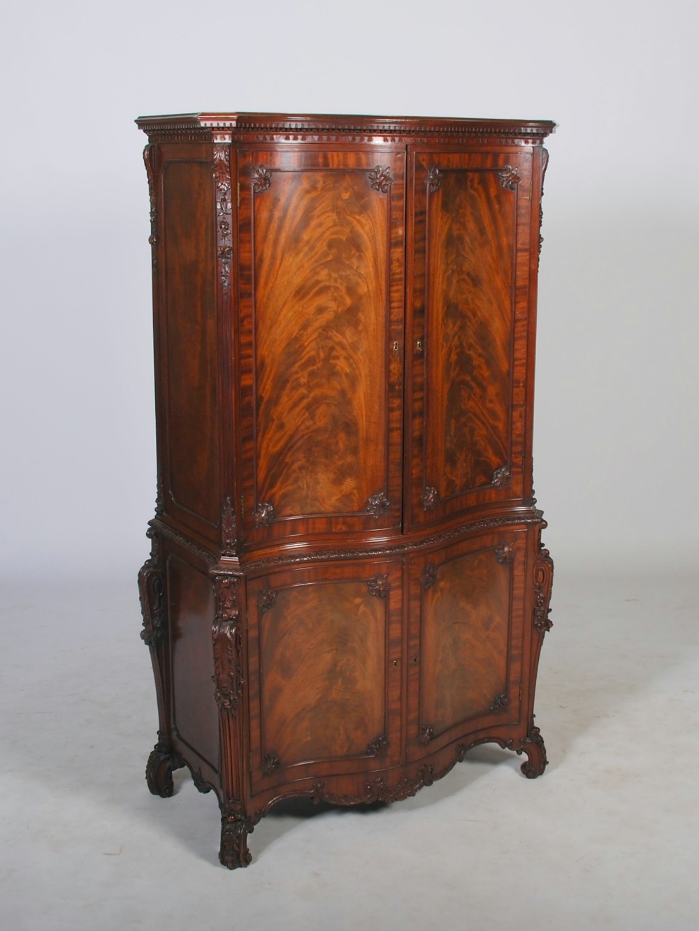 A George III style mahogany serpentine cupboard, the moulded cornice and dentil frieze above a