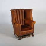 An early 20th century leather upholstered wing armchair, with brass studded details and loose velvet