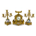 A late 19th century French gilt metal clock garniture with a rams head urn over a circular enamelled