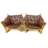 A pair of tub-style lounge chairs, the beech frames suspending the brown leather and button backed