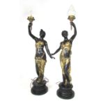 A pair of bronzed brass floor standing figural lamps cast as scantily clad maidens holding up a