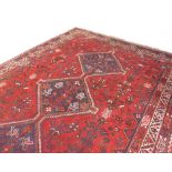 An Iranian carpet, triple lozenge medallion on a red ground with stylized flowers and birds inside a