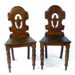 A pair of Victorian oak hall chairs with pierced and carved backs incorporating a cartouche over