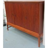 DANISH SIDE CABINET ON STAND, with three panelled cupboard doors below enclosing shelves,