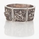 An Eastern silver bangle composed of tapering panels, each with embossed detail of Burmese