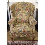 A Victorian-style mahogany framed wingback armchair with floral fabric upholstery, raised on