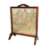 An early 20th century oak framed fire screen with multicoloured embroidered scene, raised on trestle