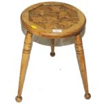 An early 20th century hardwood three legged stool with profuse foliate carving to the seat