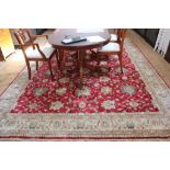 A Middle Eastern-style red ground drawing room carpet with floral and foliate depictions with a