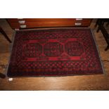 A Middle Eastern-style red ground hand knotted wool rug with short fringe and isometric designs,