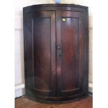 A 19th century oak stained convex hanging corner cupboard with twin doors, revealing a shelved