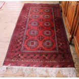 A Persian red-ground hand knotted wool rug with treble border, multicoloured isometric designs